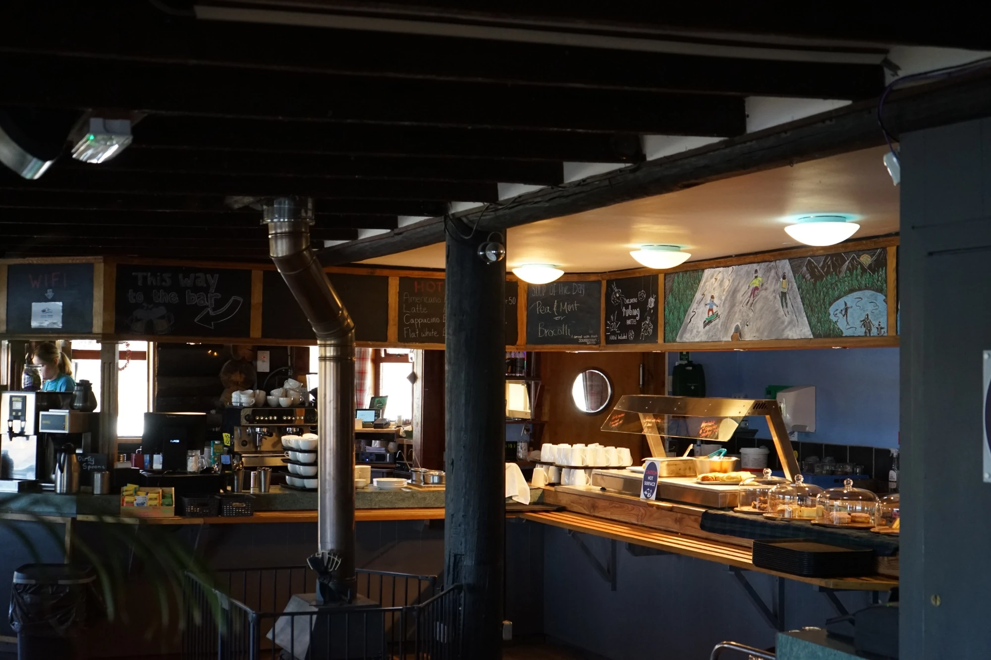 Cozy café interior with a rustic vibe, featuring a counter with an array of baked goods. Chalkboard menus hang above, adding a warm, inviting feel.