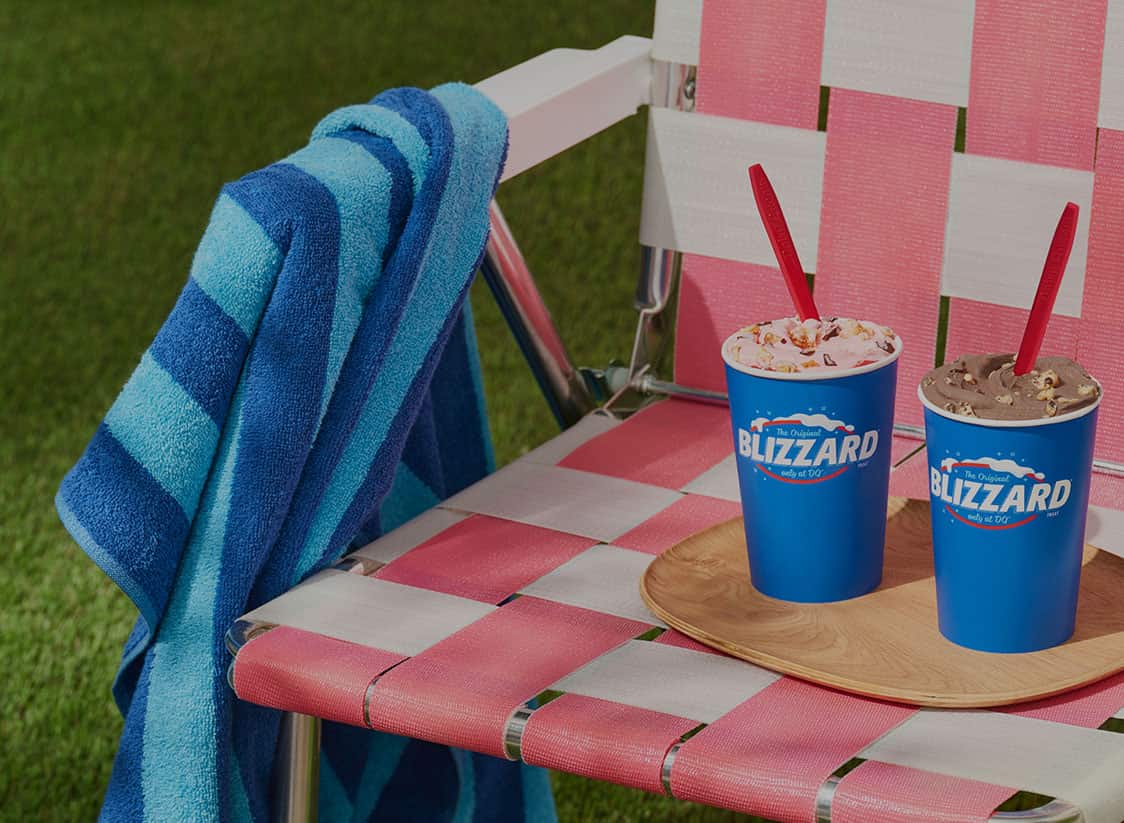 WTADS client DQ two Blizzards in blue cups sitting on retro pink chair with blue beach towel in grass.