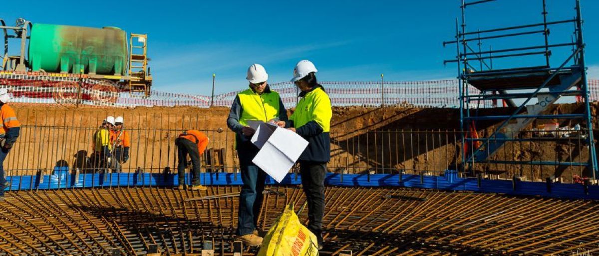 UMINEX engineers reviewing construction plans at an infrastructure site beside rebar and formwork.