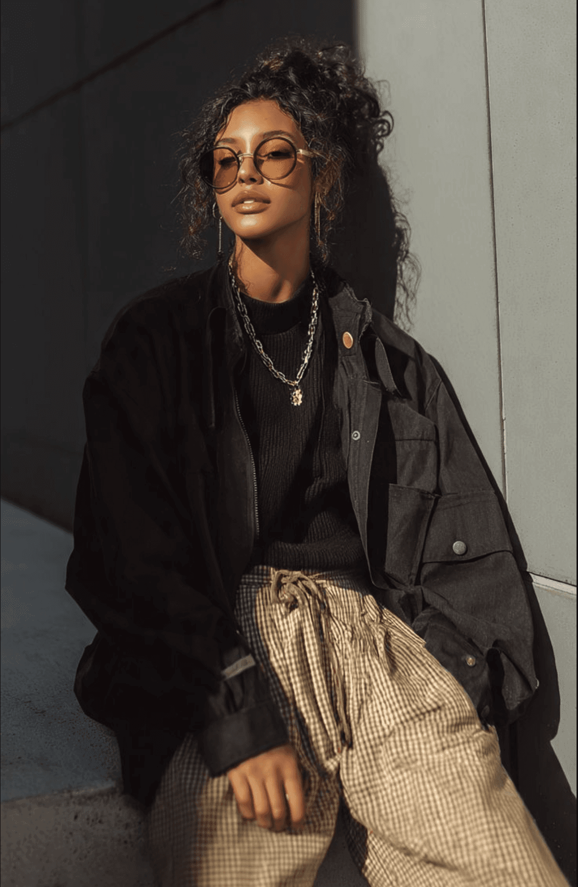 A woman in a teal dress sits in a dimly lit room, focused on her smartphone. A laptop and notepad are on the glass table, suggesting a working environment.