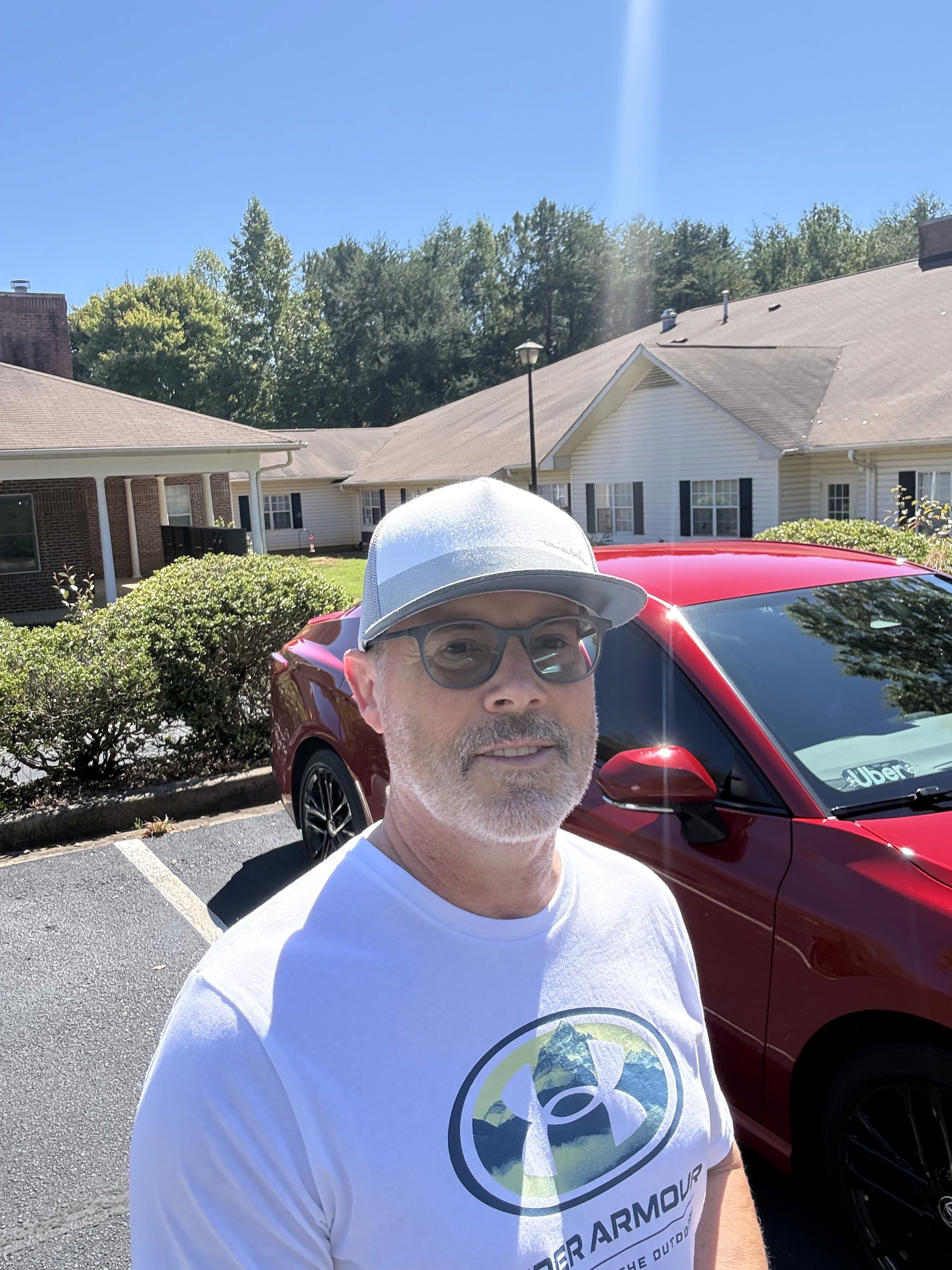 Stuart standing in front of his red Camry, with bushes and a building in the background.