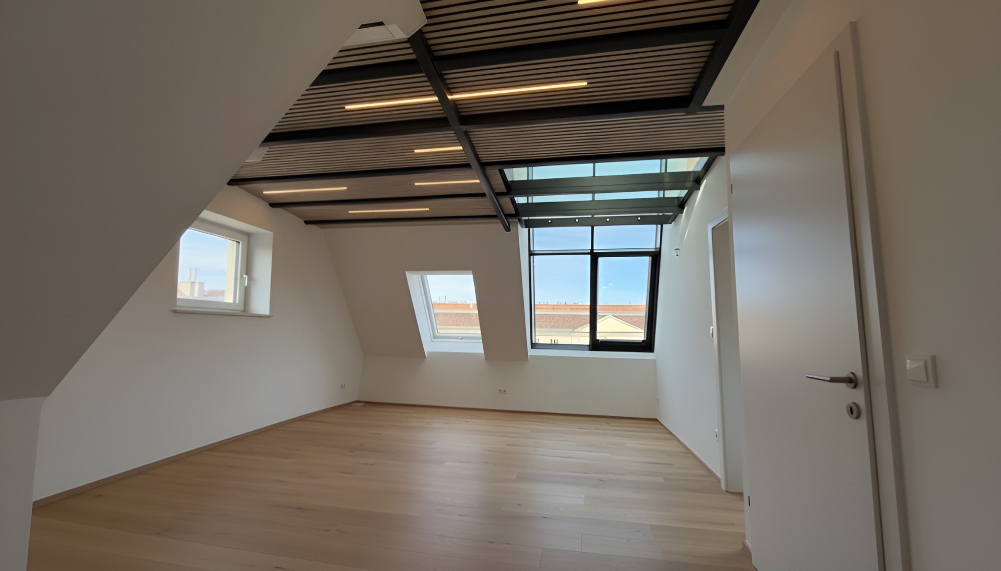 Moderner Dachausbau in Wien mit Akustikdecke und großem Fenster für natürliches Licht.