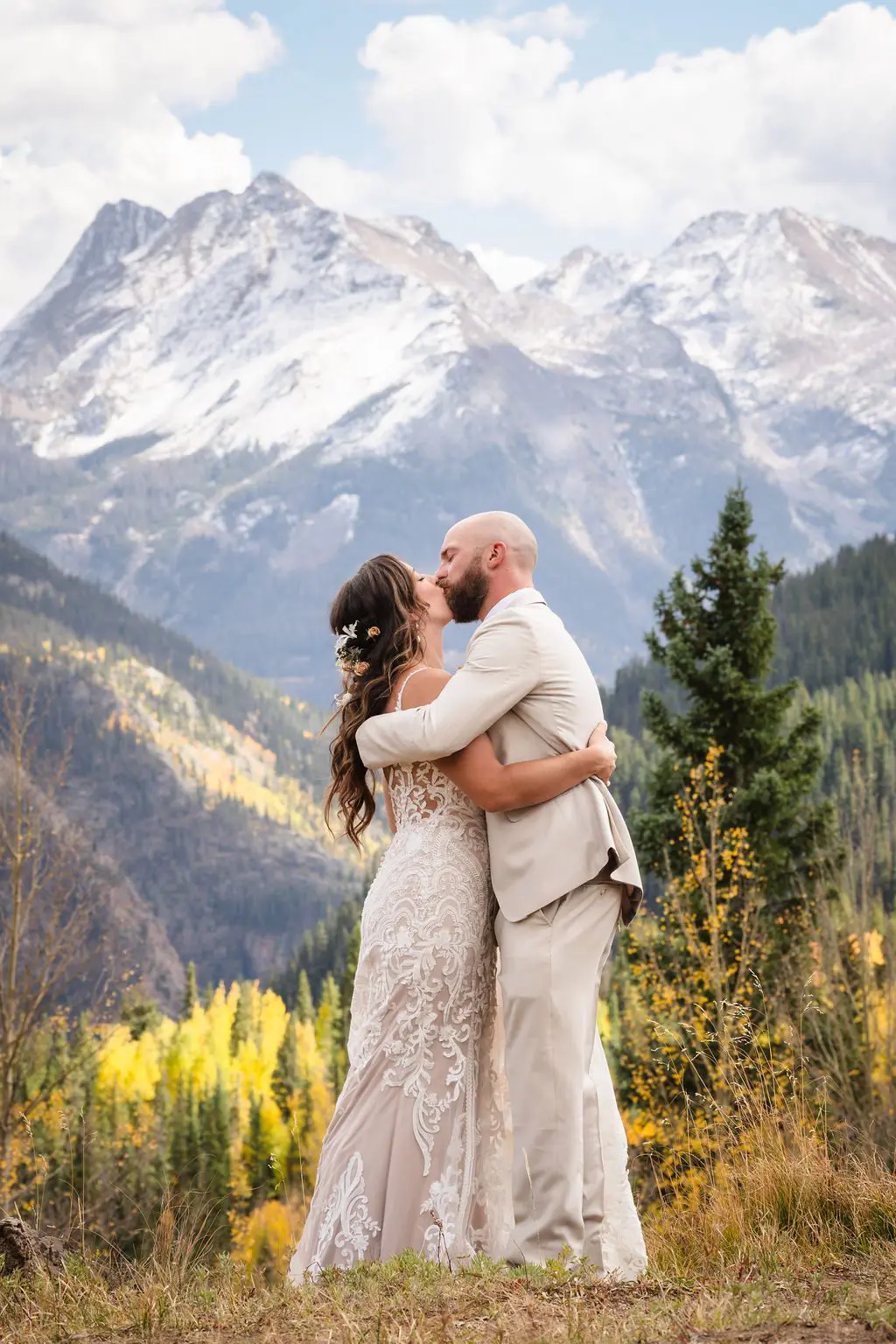 A bride and groom share a romantic kiss against the breathtaking backdrop of the San Juan Mountains, captured by a Silverton Colorado wedding photographer. The couple is surrounded by golden autumn aspens and snow-capped peaks.