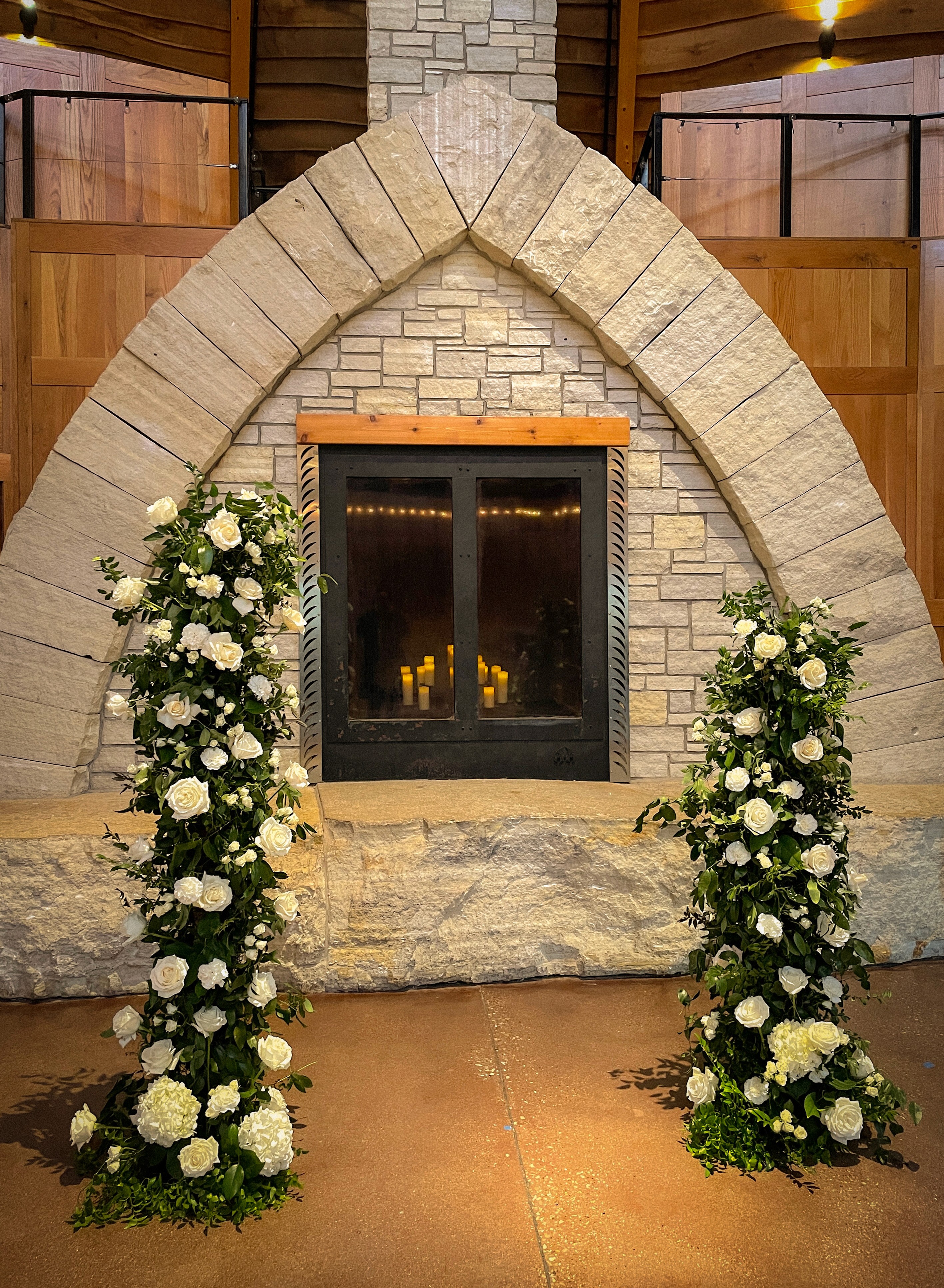 Indoor wedding fireplace with white floral aisle arrangements by Des Moines Iowa florist.