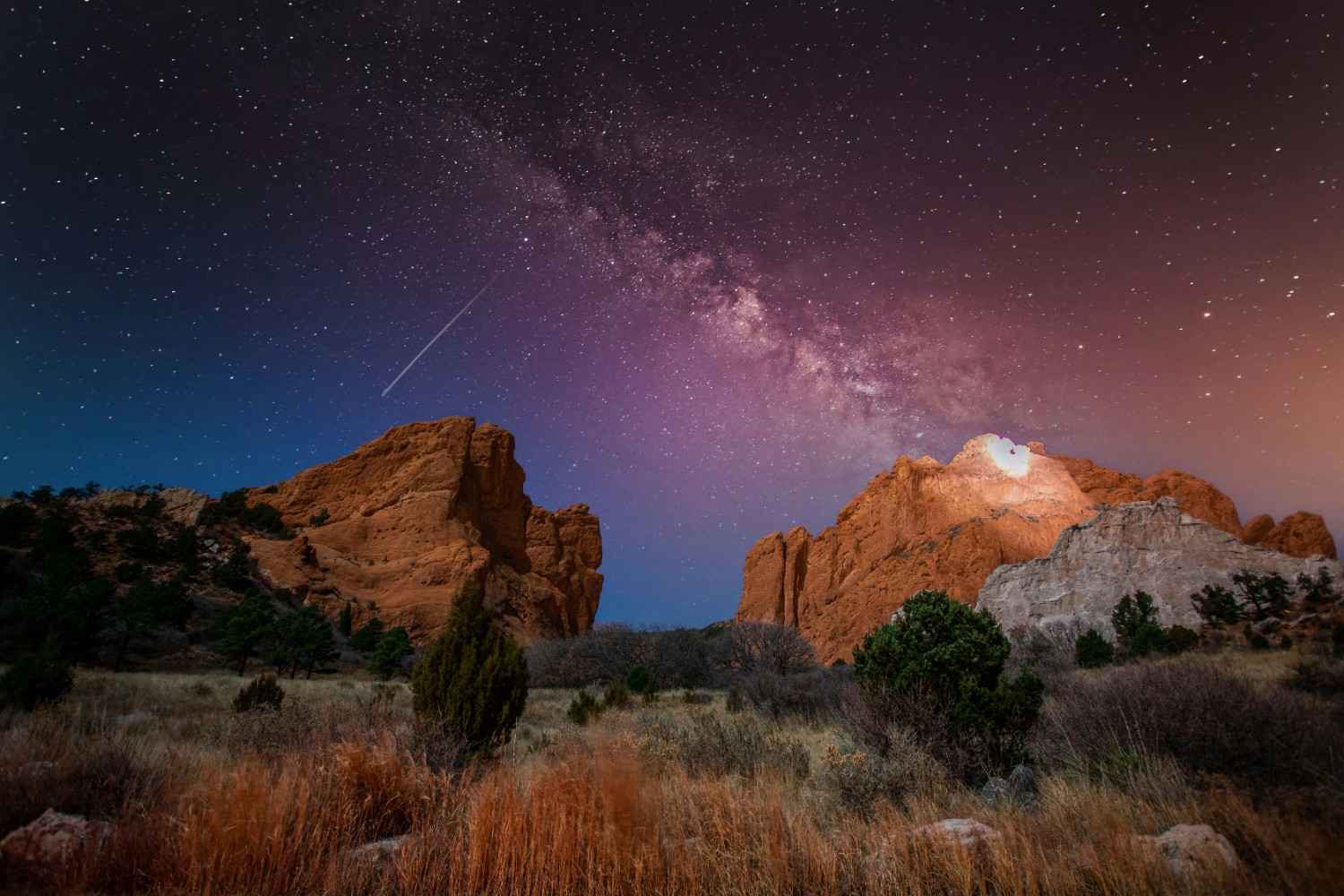 Desert landscape at night with illuminated rock formations and a star-filled sky