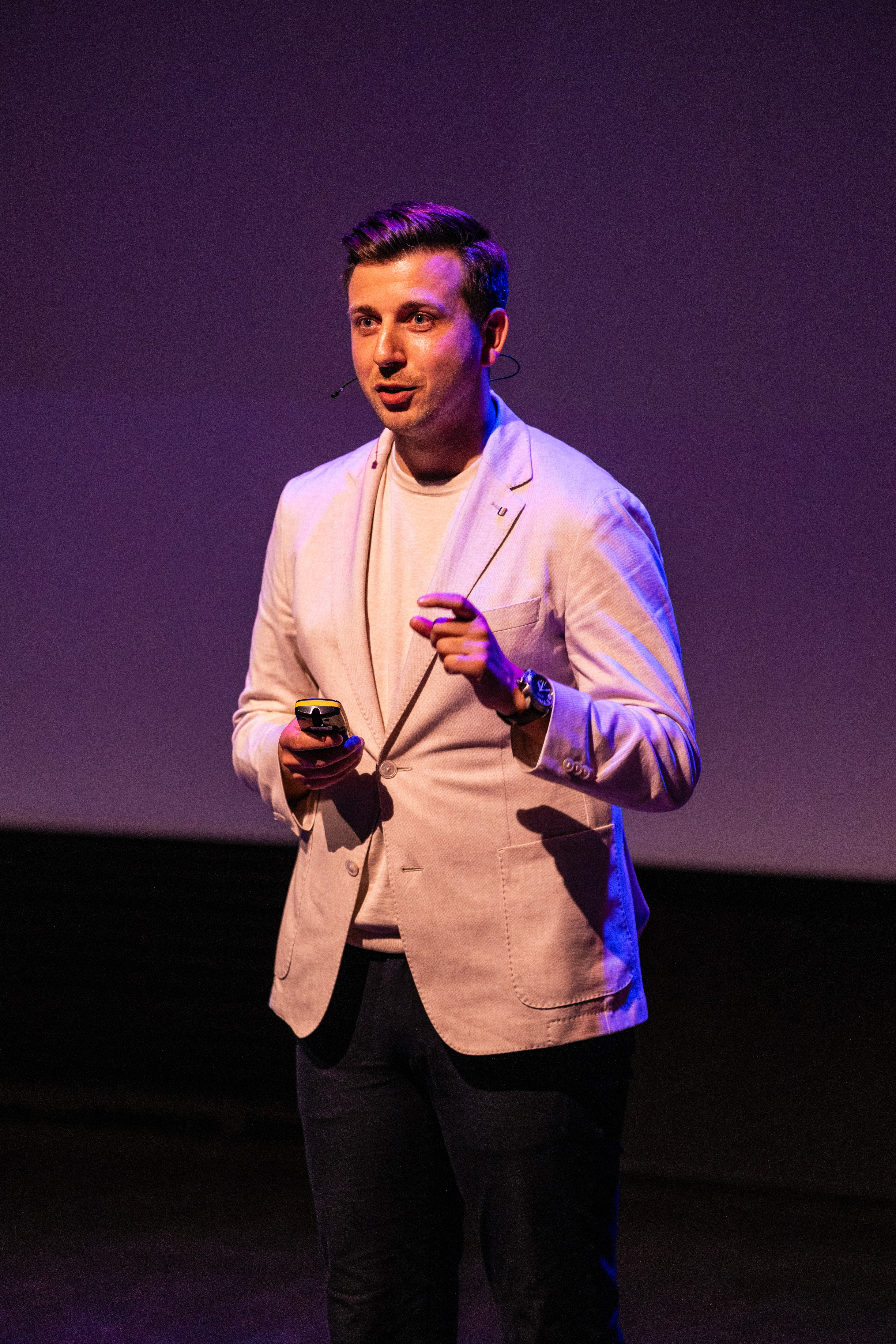 A smiling woman with her arms crossed, standing against a dark green background. She has long, dark hair.
