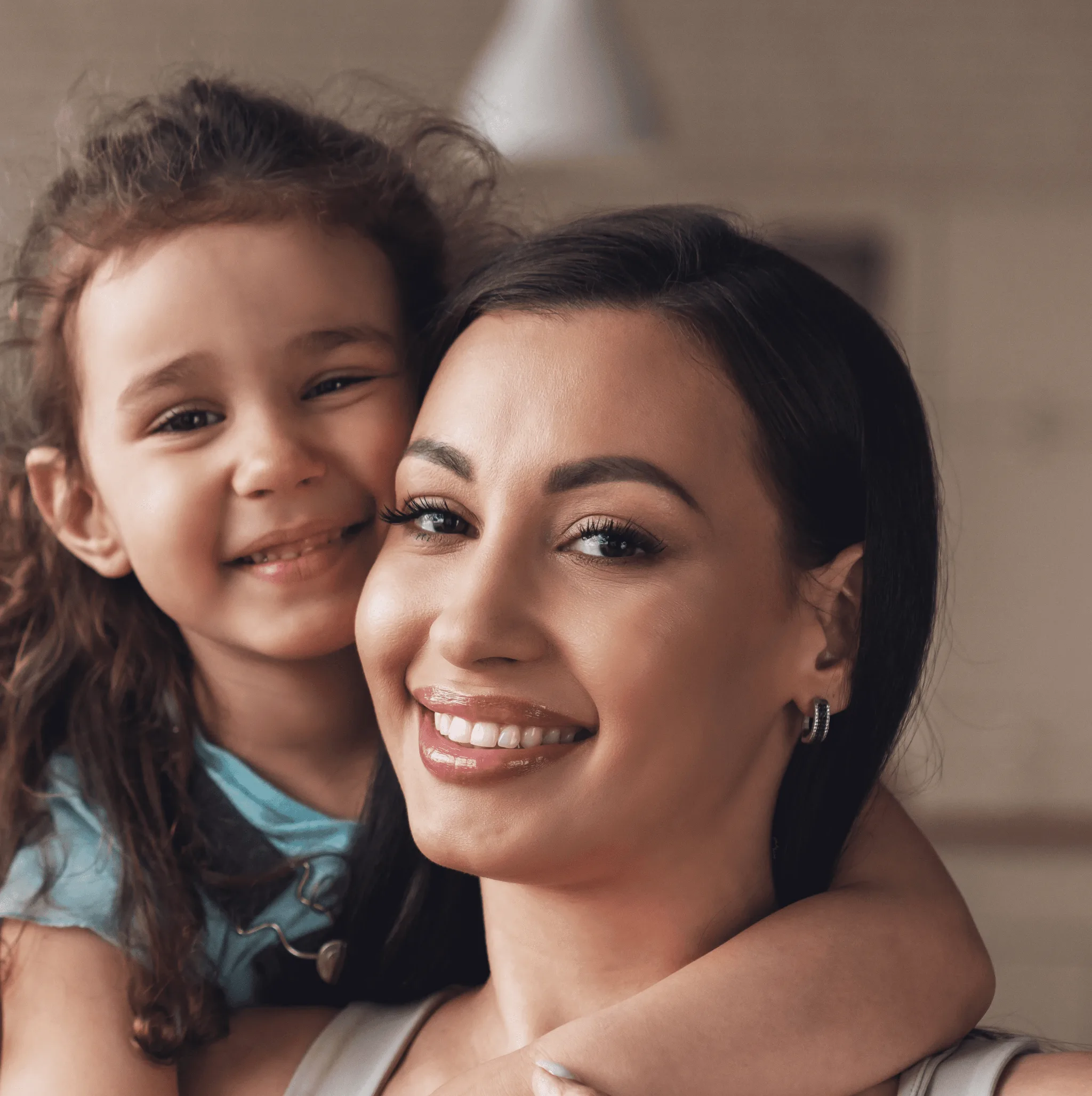 Mom smiling at camera, with her daughter hugging her from behind.