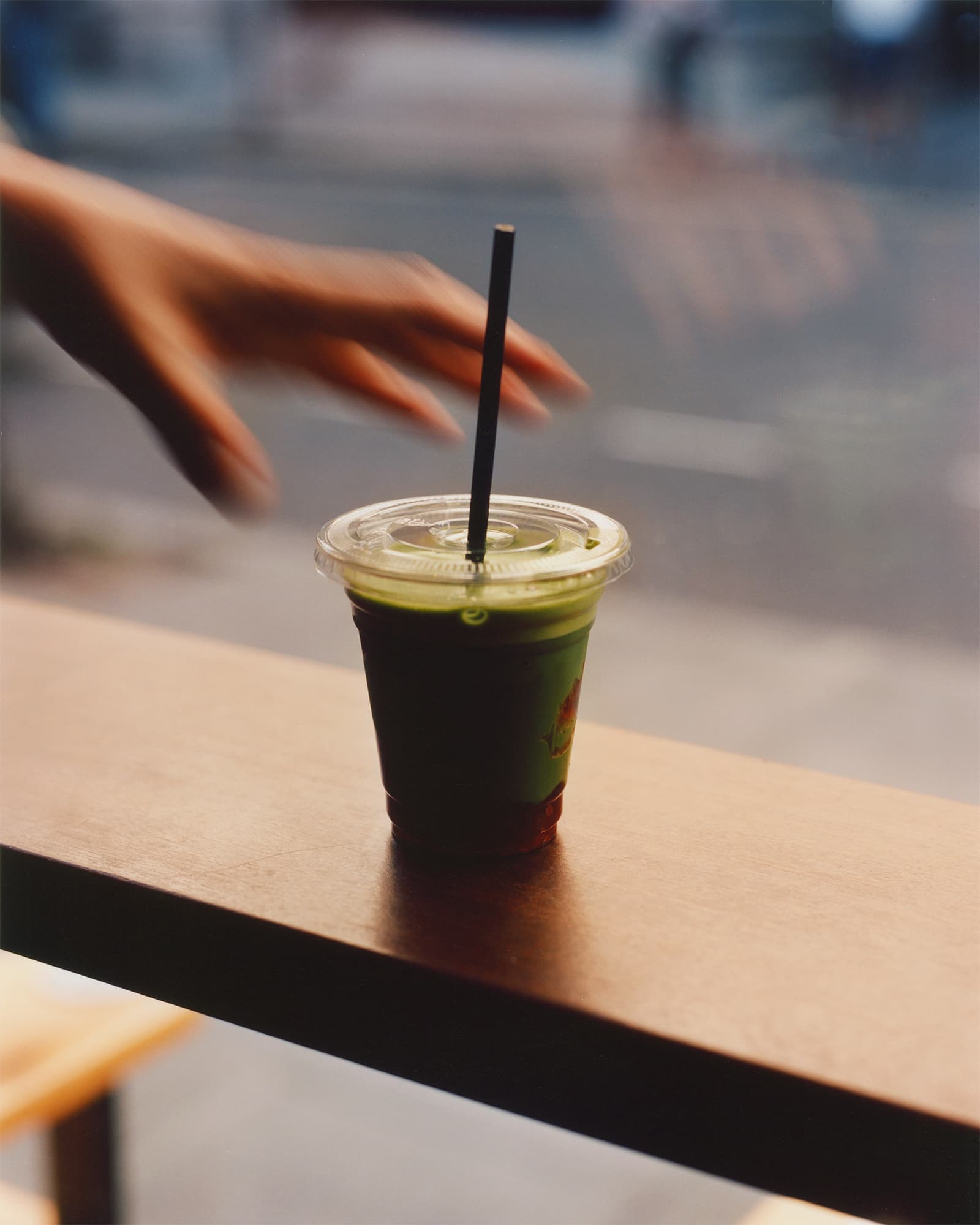 A human hand about to grab a green cup inside NKORA Coffee Shop