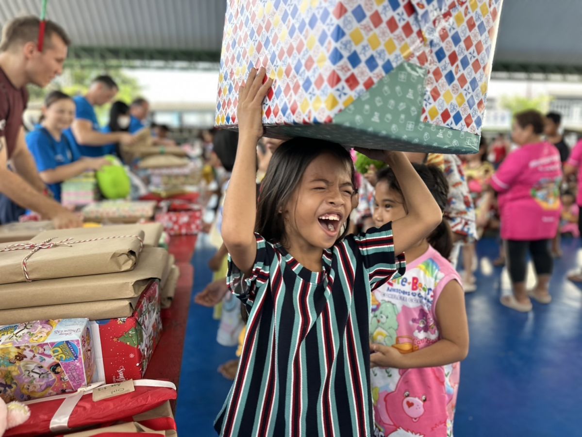 man in blue t-shirt and white floral skirt holding black smartphone while sitting on sidewalk