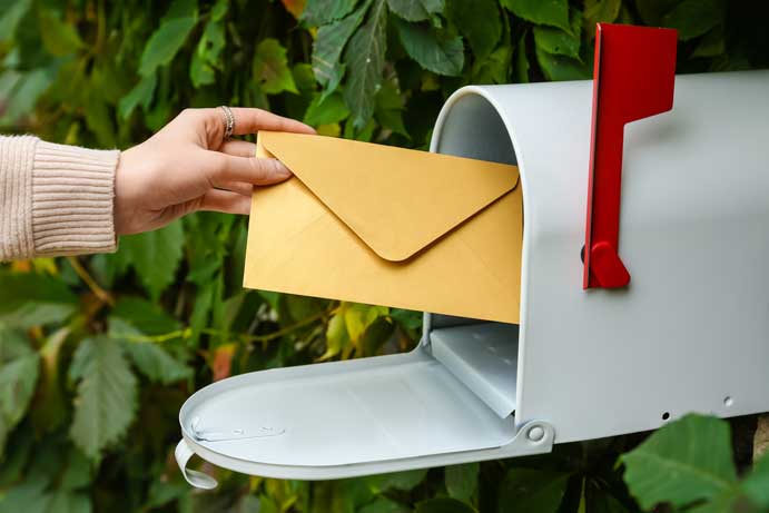 A hand placing a letter into a mailbox.