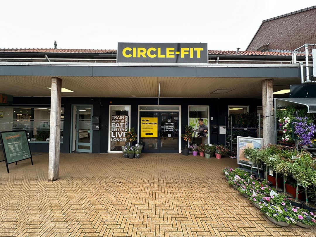 A Circle Fit hub with large windows, a sign above, and a path lined with plants and flowers in front.