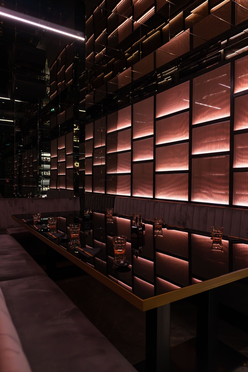 Elegant dining scene with a round table set for two, featuring a white tablecloth, three lit candles, and blue velvet chairs in a dimly-lit, plush setting.