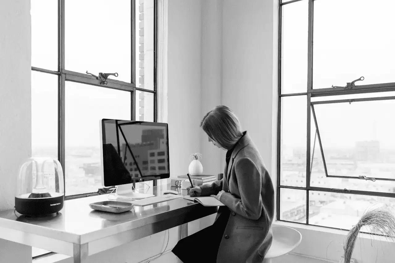 A black and white photo of a professional woman working at a desk with a computer