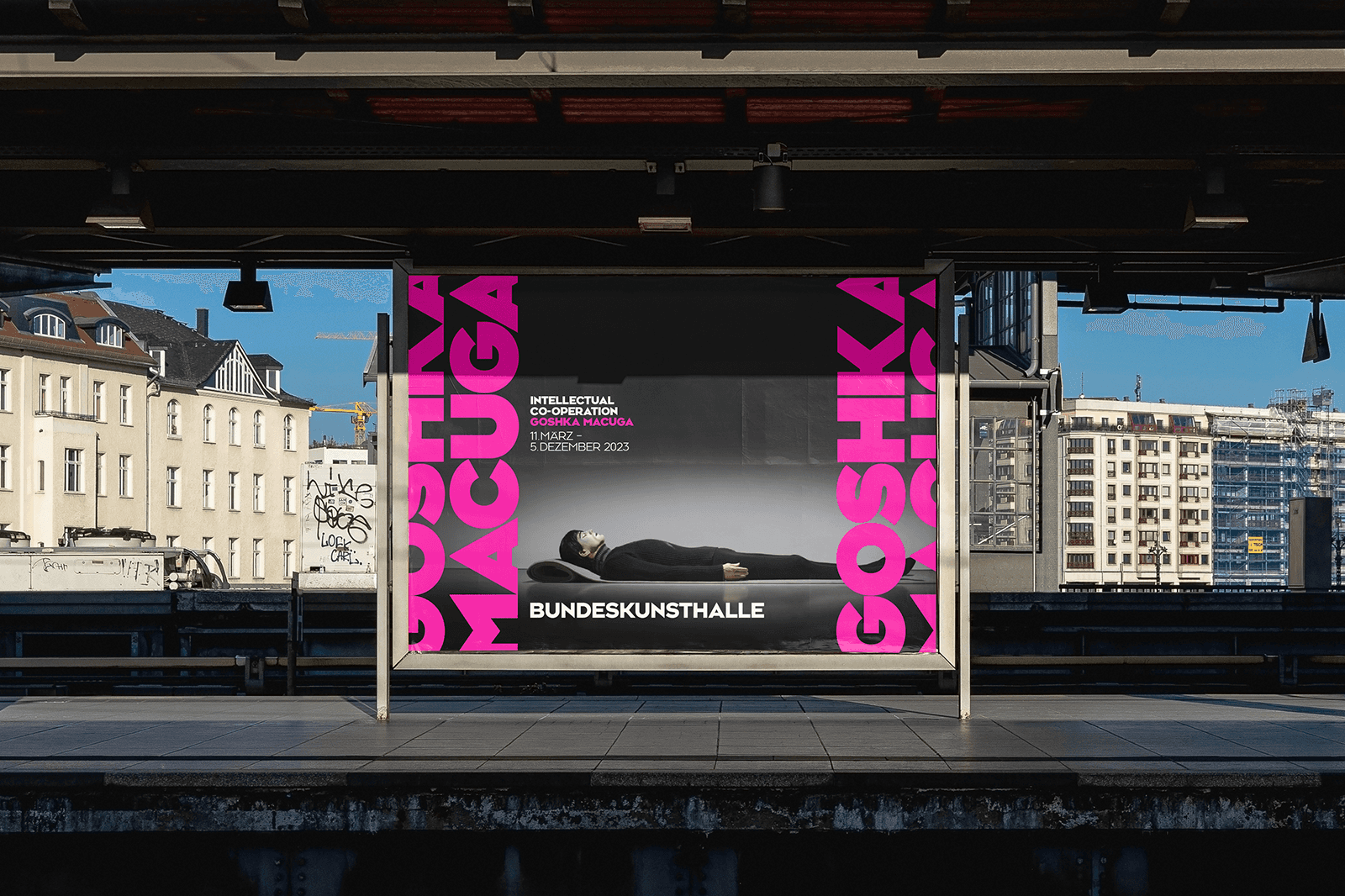 A vibrant pink display stands in front of a gray backdrop, set in an urban environment.