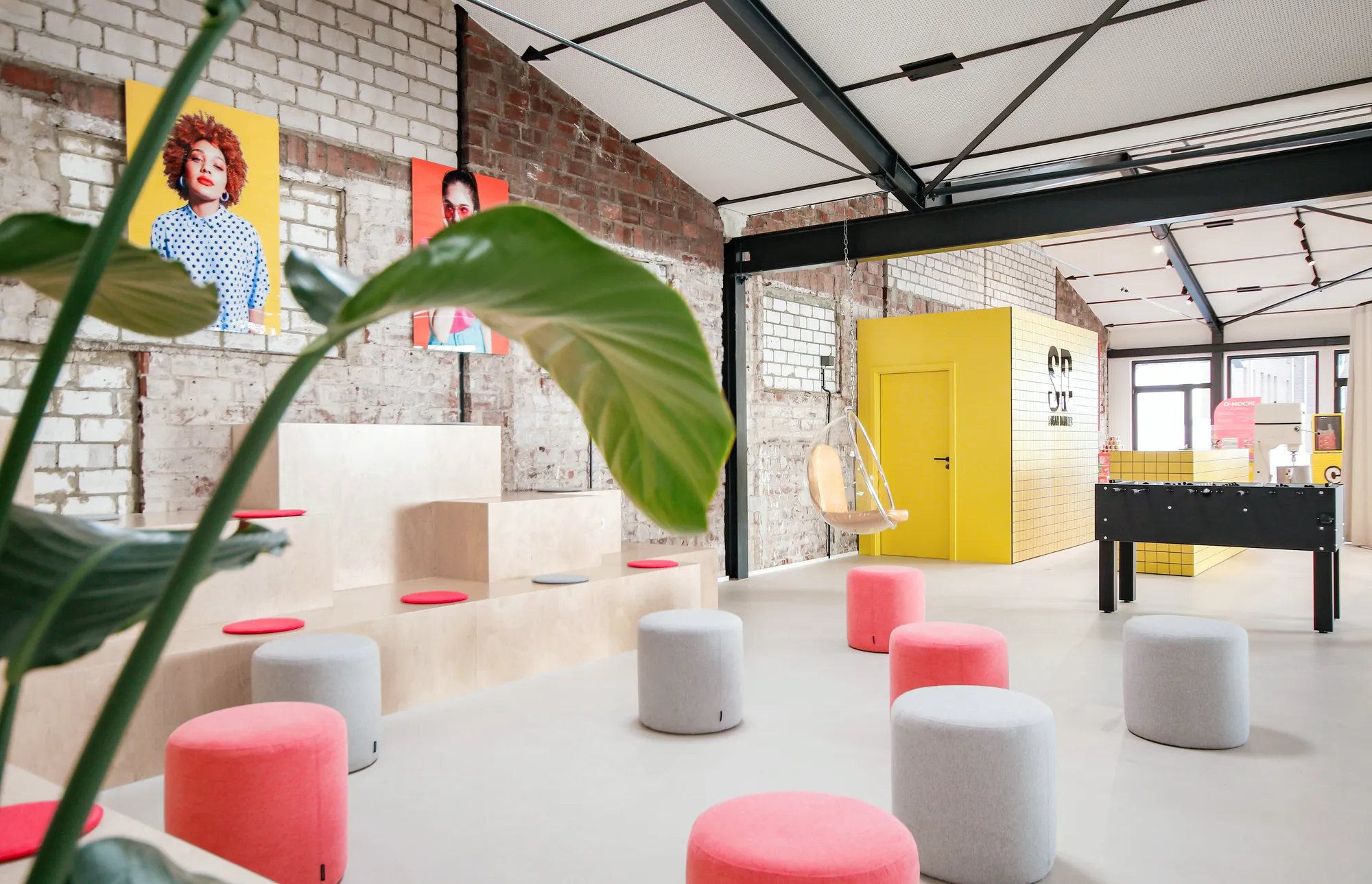Brick-walled lounge with pink and grey poufs, foosball table and pop-art portraits.
