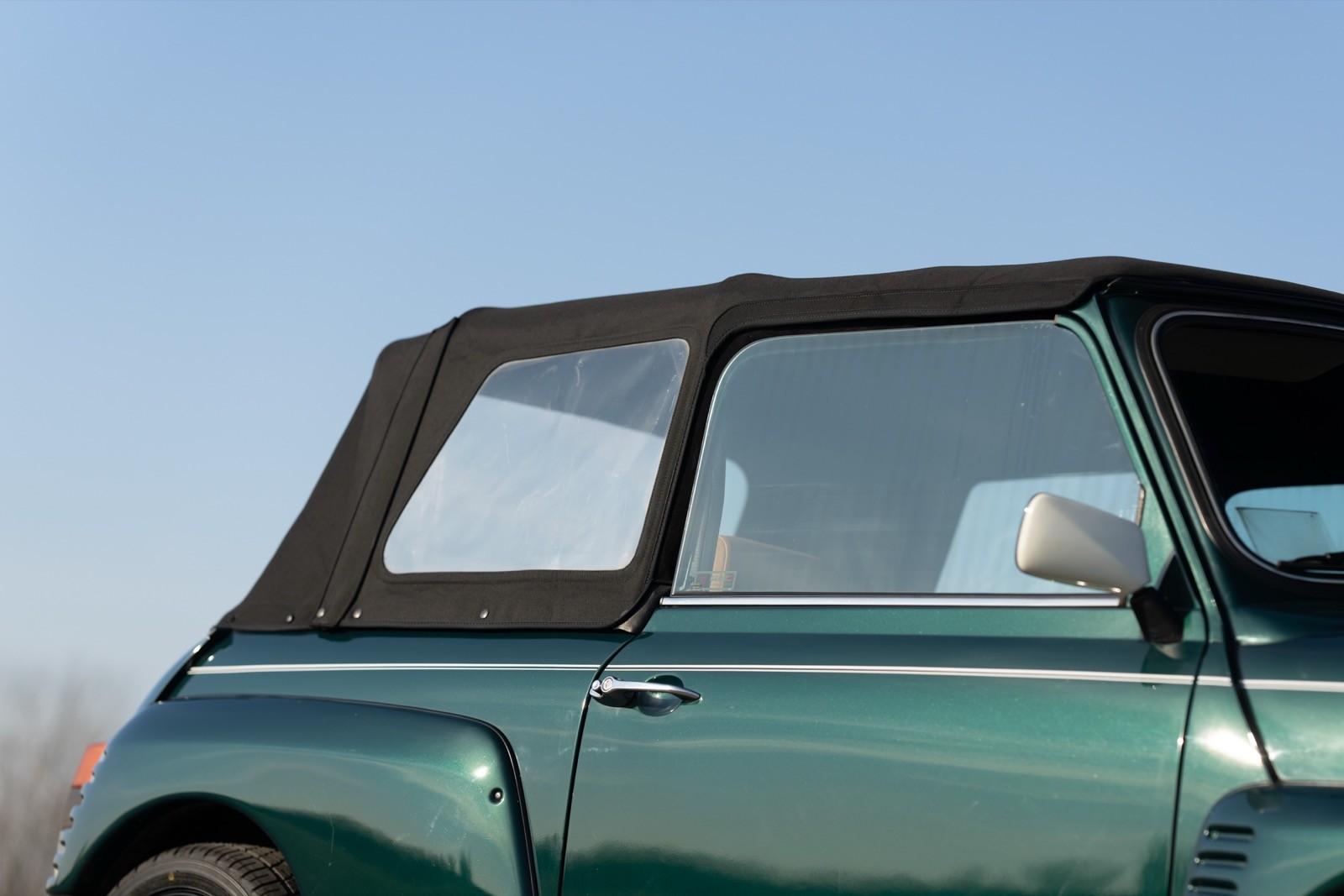 A close-up of a green convertible car with a black soft top against a clear blue sky.