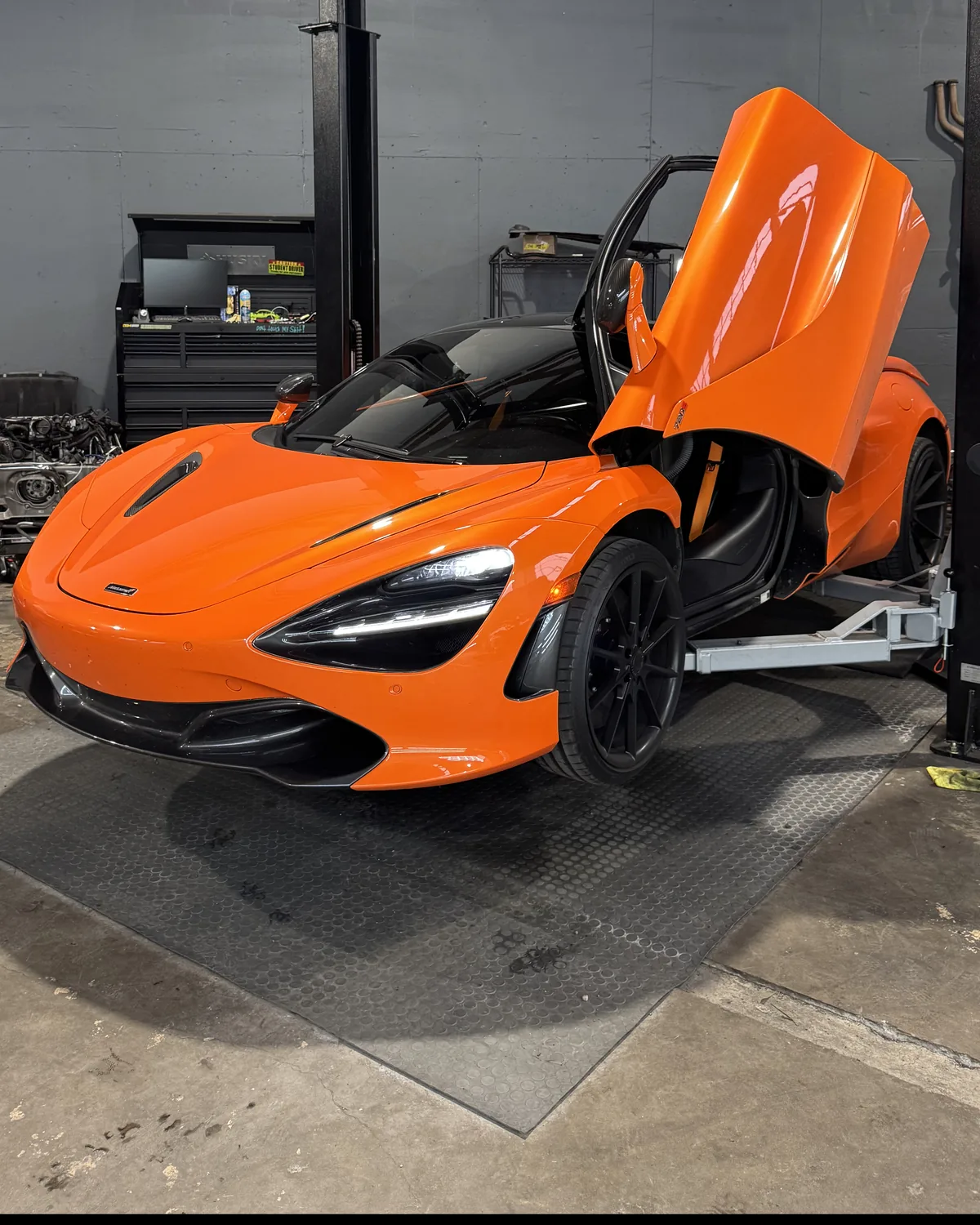 Orange McLaren 720S with its doors up beside a lift in the 714 Technik service bay