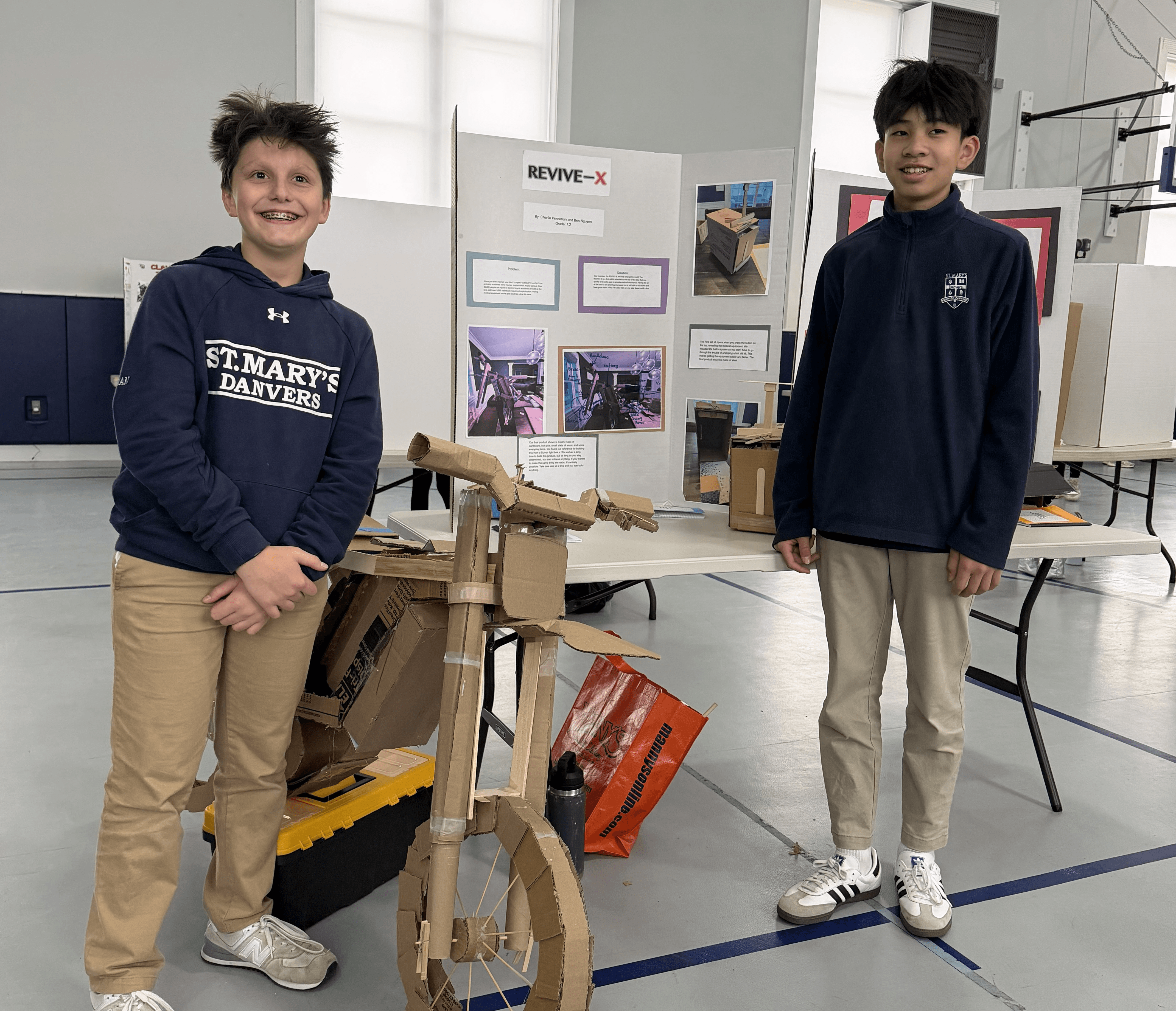 Two students beside their invention fair display and cardboard motorcycle model