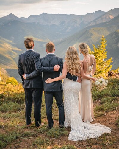 The newlyweds and two members of their wedding party stand together facing the mountains.