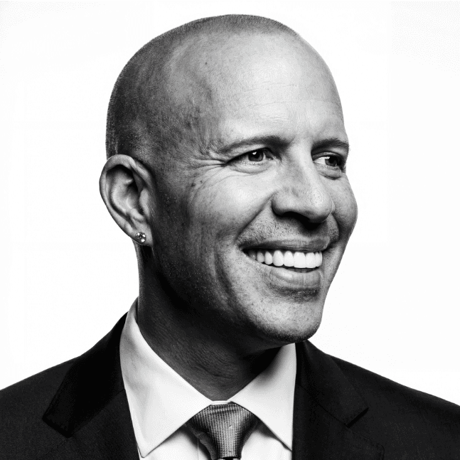 Portrait of a business man with straight white teeth, set against a neutral backdrop.