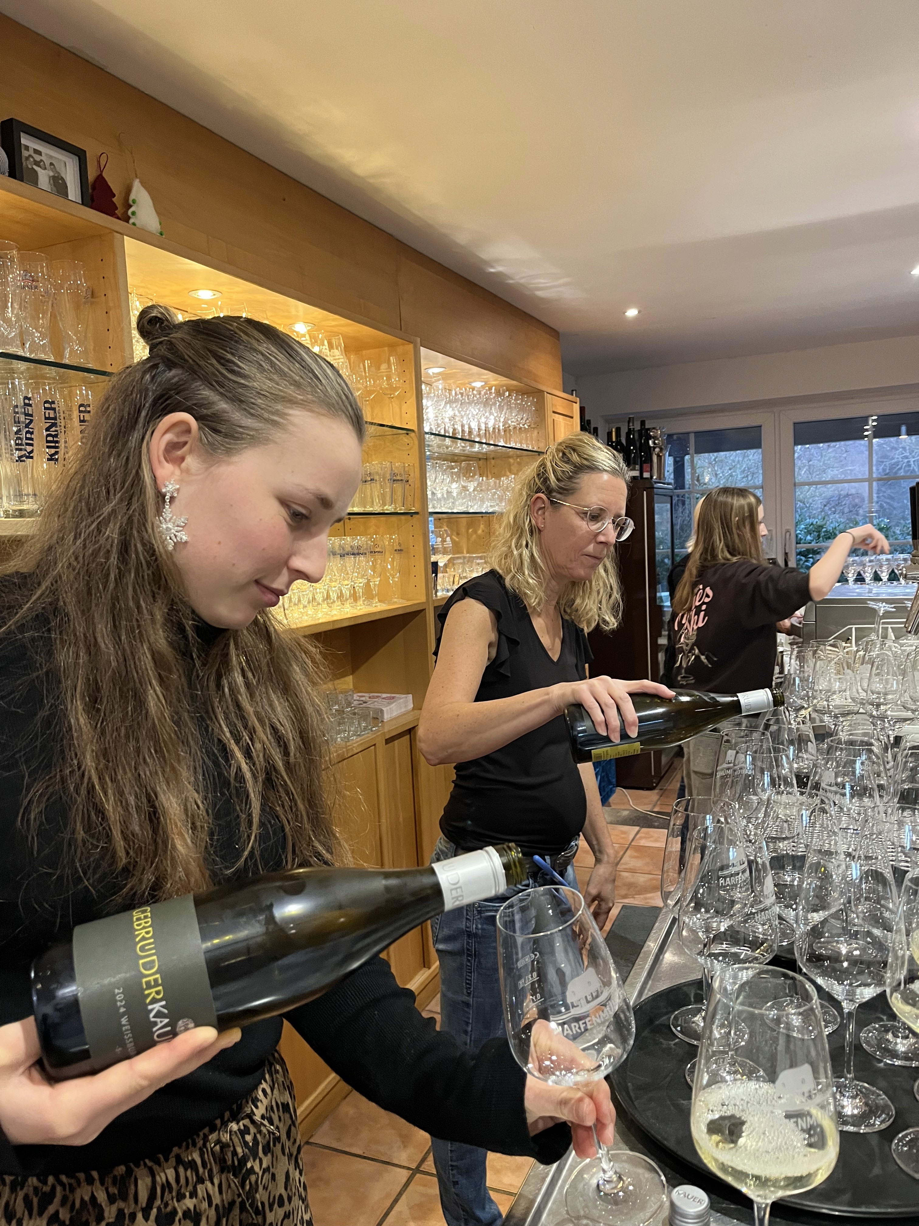 Claire und Tanja füllen die Weingläser an der Theke mit Weißwein.