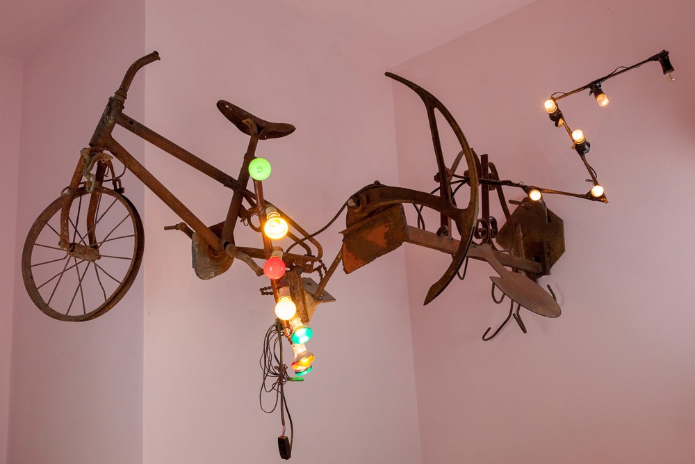 Two bicycles creatively mounted on a wall, adorned with decorative lights, against a pink background.
