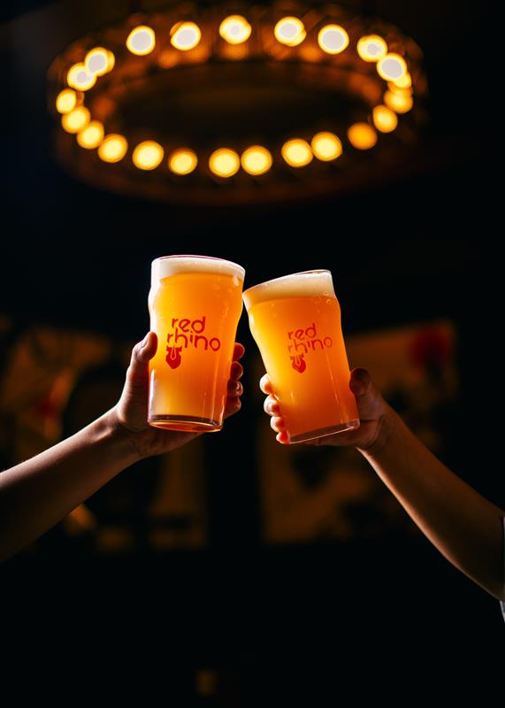 Two people toasting Red Rhino craft beers under warm bar lighting