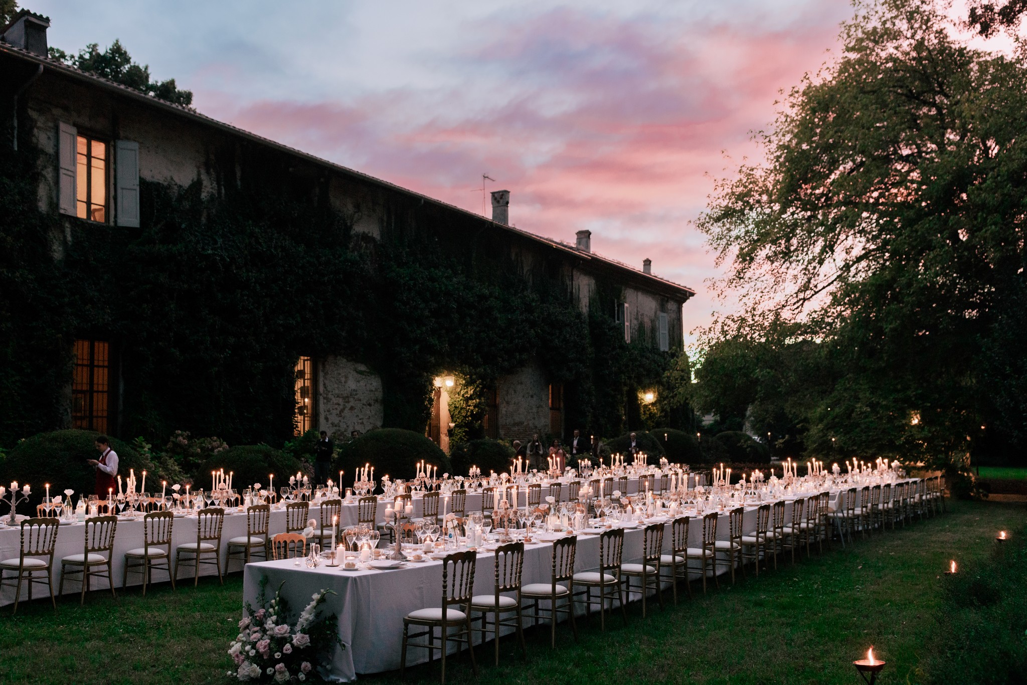 Ricevimento matrimoniale al tramonto nel giardino di Villa Ferrari, tavoli illuminati da candele e villa storica