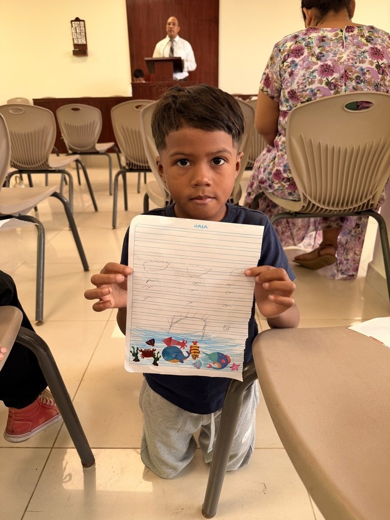 A child holding up a craft in a gathering room.