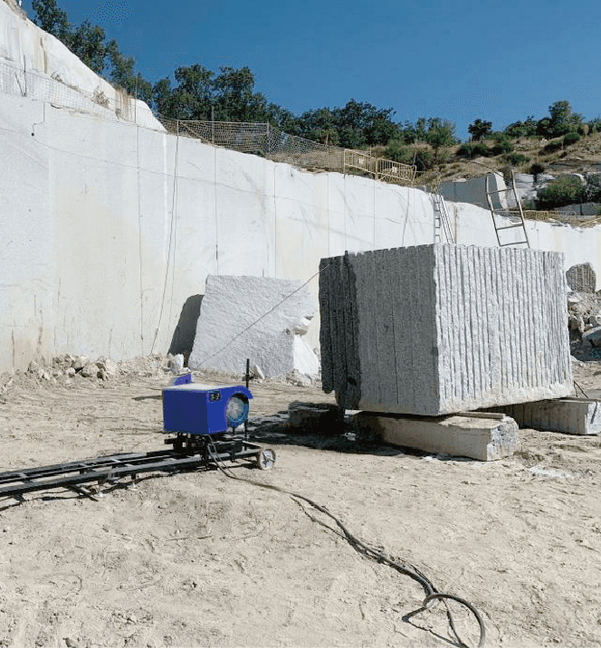 Portable trimming wire saw machine positioned near a large stone block in a quarry, illustrating its capability to handle substantial stone sizes and easy maneuverability.