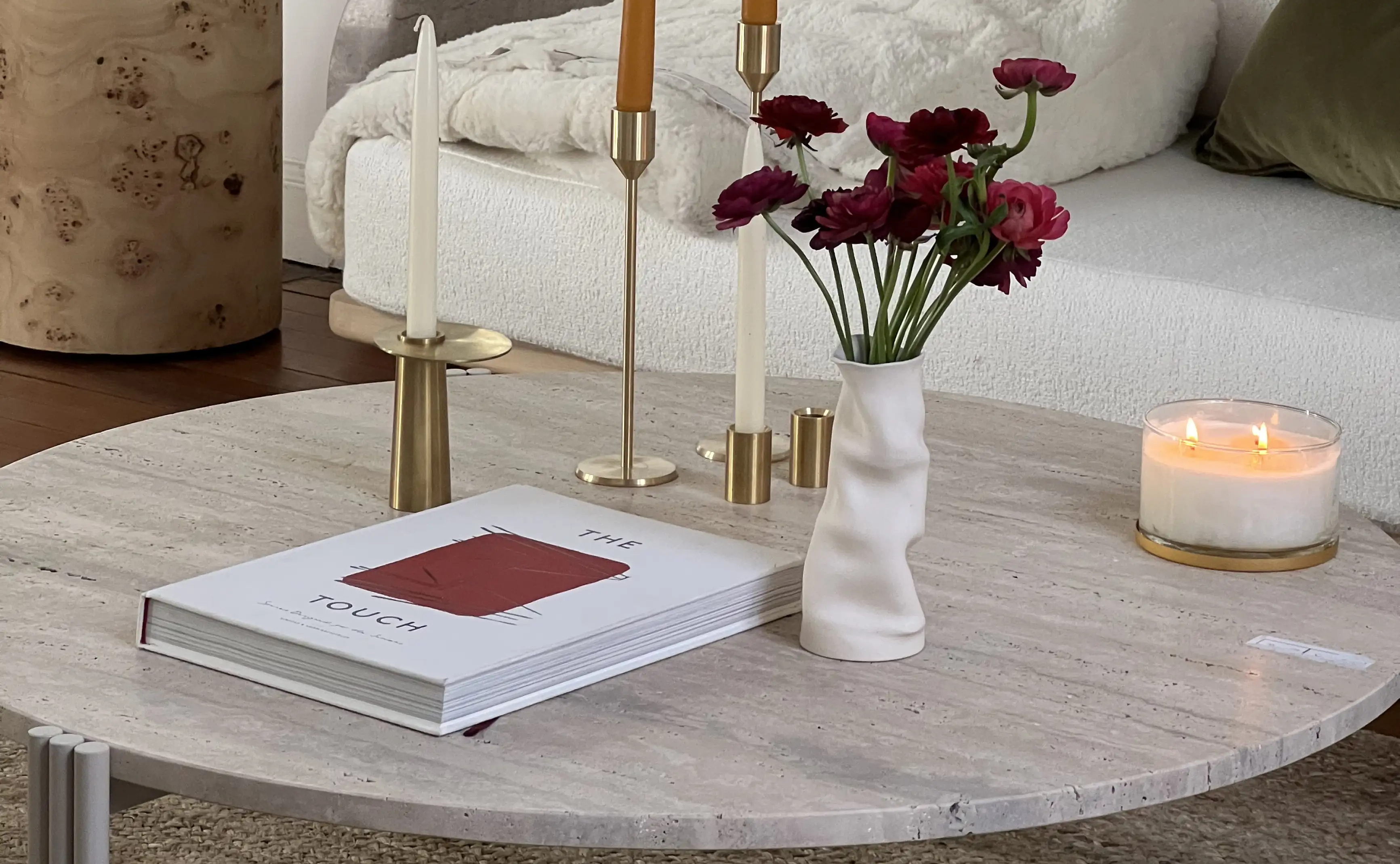Composición de mesa baja con flores rojas, velas y libro de diseño para marcas de interiorismo que comunican calidez y estilo contemporáneo.