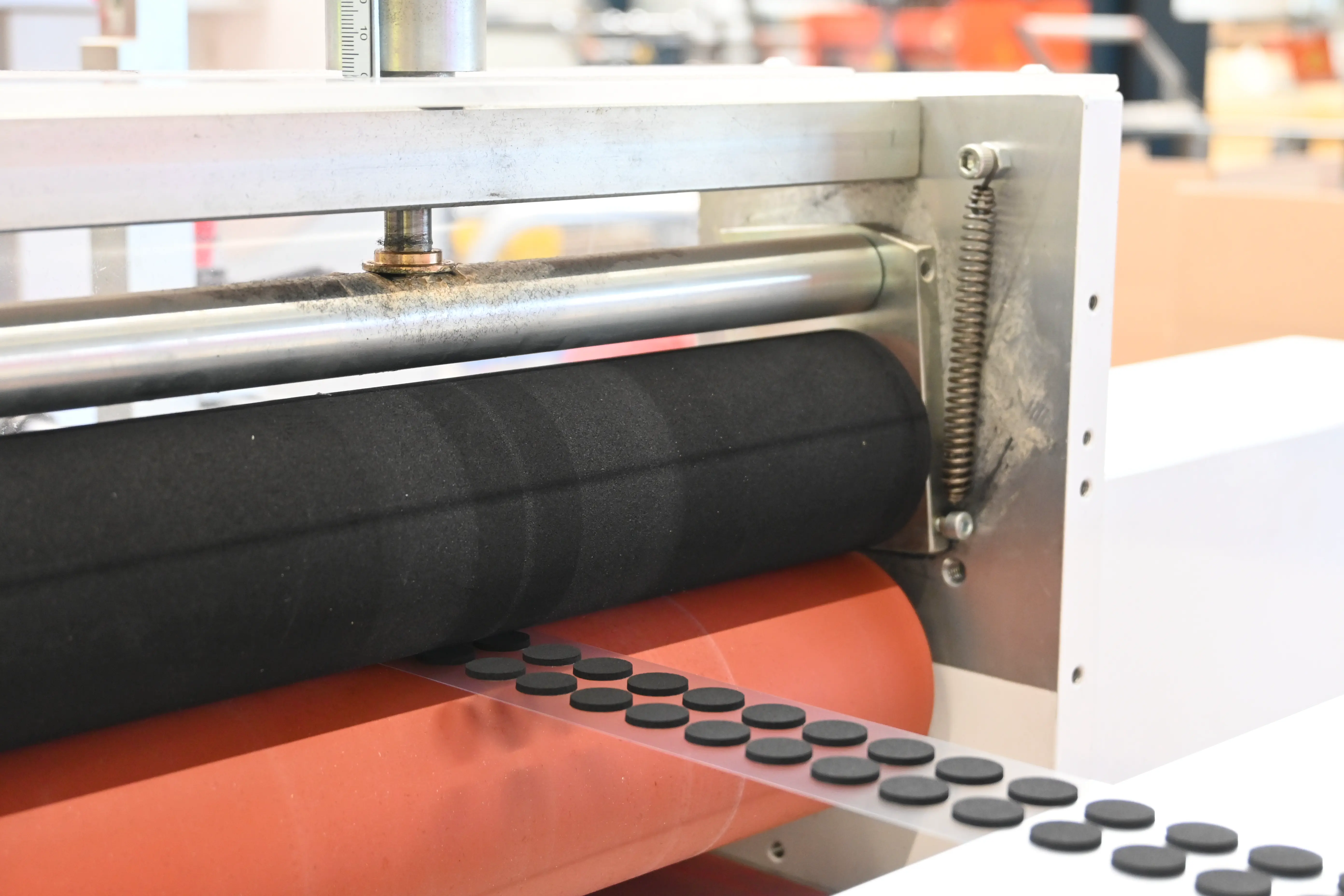 Nahaufnahme einer Maschinenkomponente mit einer großen schwarzen Walze und einem orangefarbenen Teil in einer industriellen Umgebung.