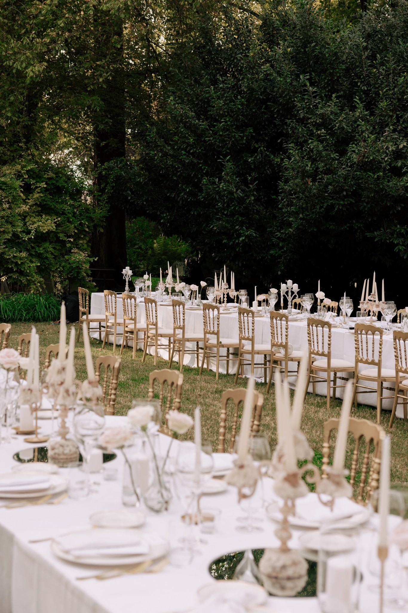 Tavoli allestiti nel parco di Villa Ferrari con sedie chiavari, bicchieri e fiori bianchi per il ricevimento di matrimonio