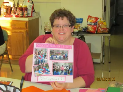 Woman holding up a pink scrapbook page of group photos