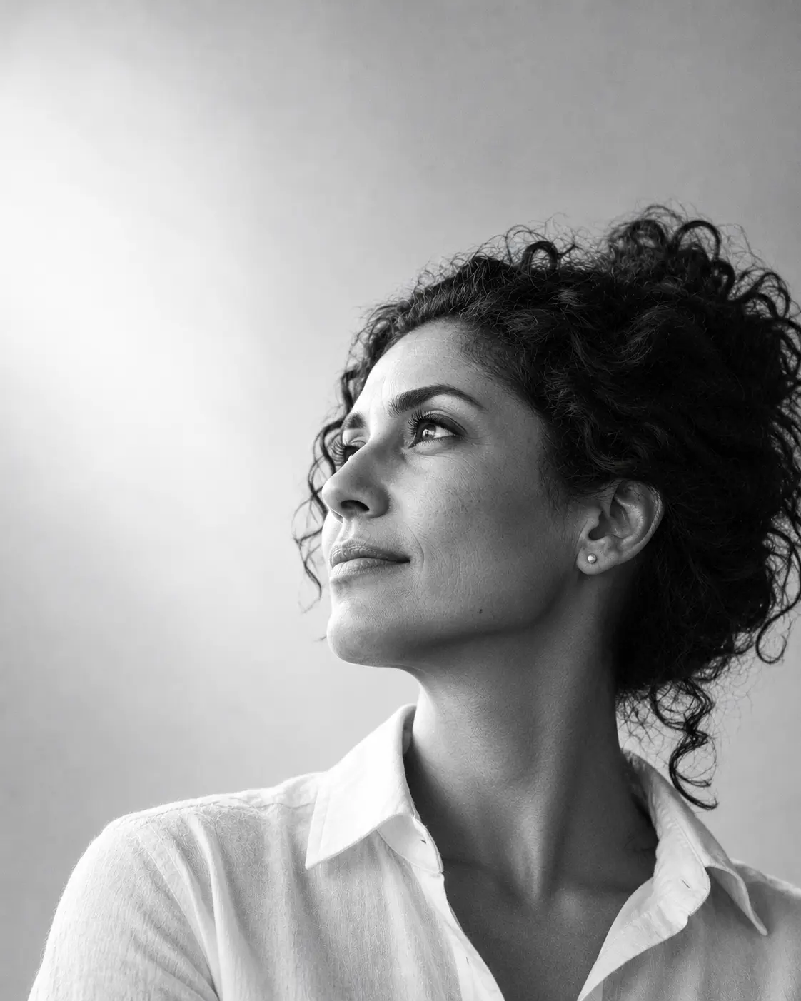 Yasmin Haddad, partner and chief investment officer, in a white open-collar shirt with curly hair worn up, looking up and to the left