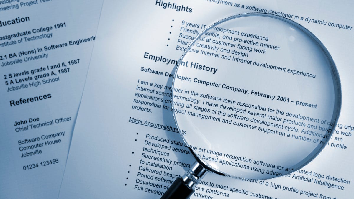 A magnifying glass on a pile of resumes