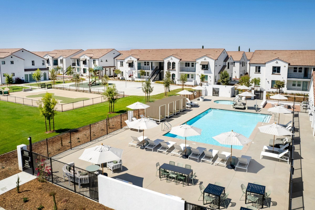 Sunny outdoor courtyard of a residential complex featuring a large swimming pool, lounge chairs, and white stucco buildings with terracotta roofs, protected by M-Fire.
