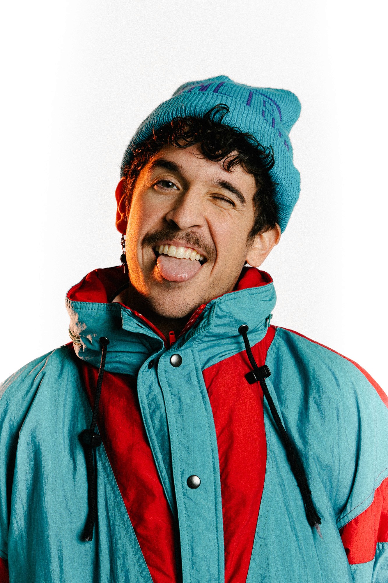 Male dancer wearing a colorful jacket and beanie winking at the camera for Momentum Art Studios
