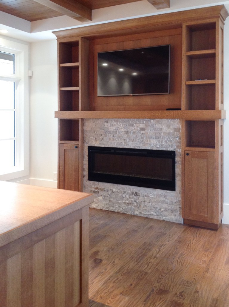 Image of Wooden built-in shelving and cabinetry surrounding a stone fireplace and mounted television in a cozy room.