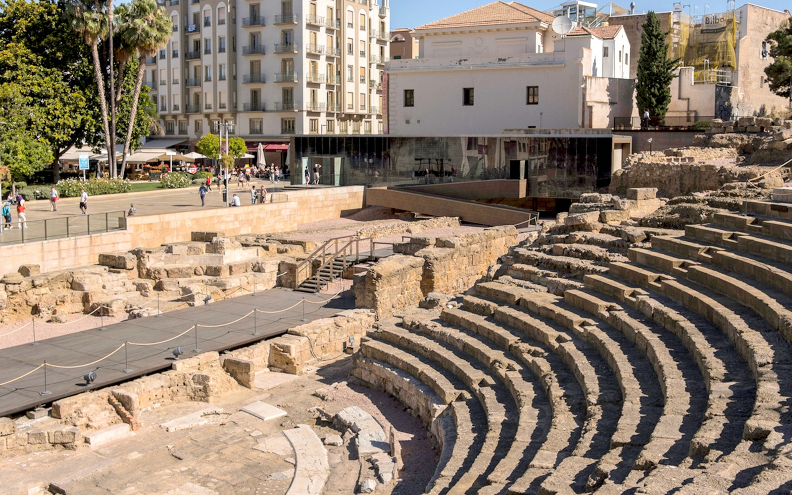 Roman Theater ruins in Málaga with nearby modern buildings and tourists exploring.