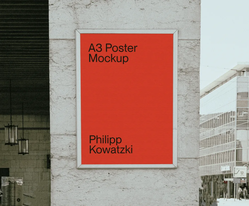 A3 poster mockup displayed in a sleek metal frame on a textured concrete wall. The setting includes urban elements, with buildings and pedestrians visible in the background.