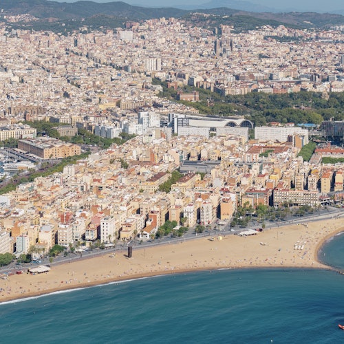 俯瞰海滨城市,密集的建筑、宽阔的沙滩和蔚蓝的海水尽收眼底。沙滩上可以看到稀疏的人群。