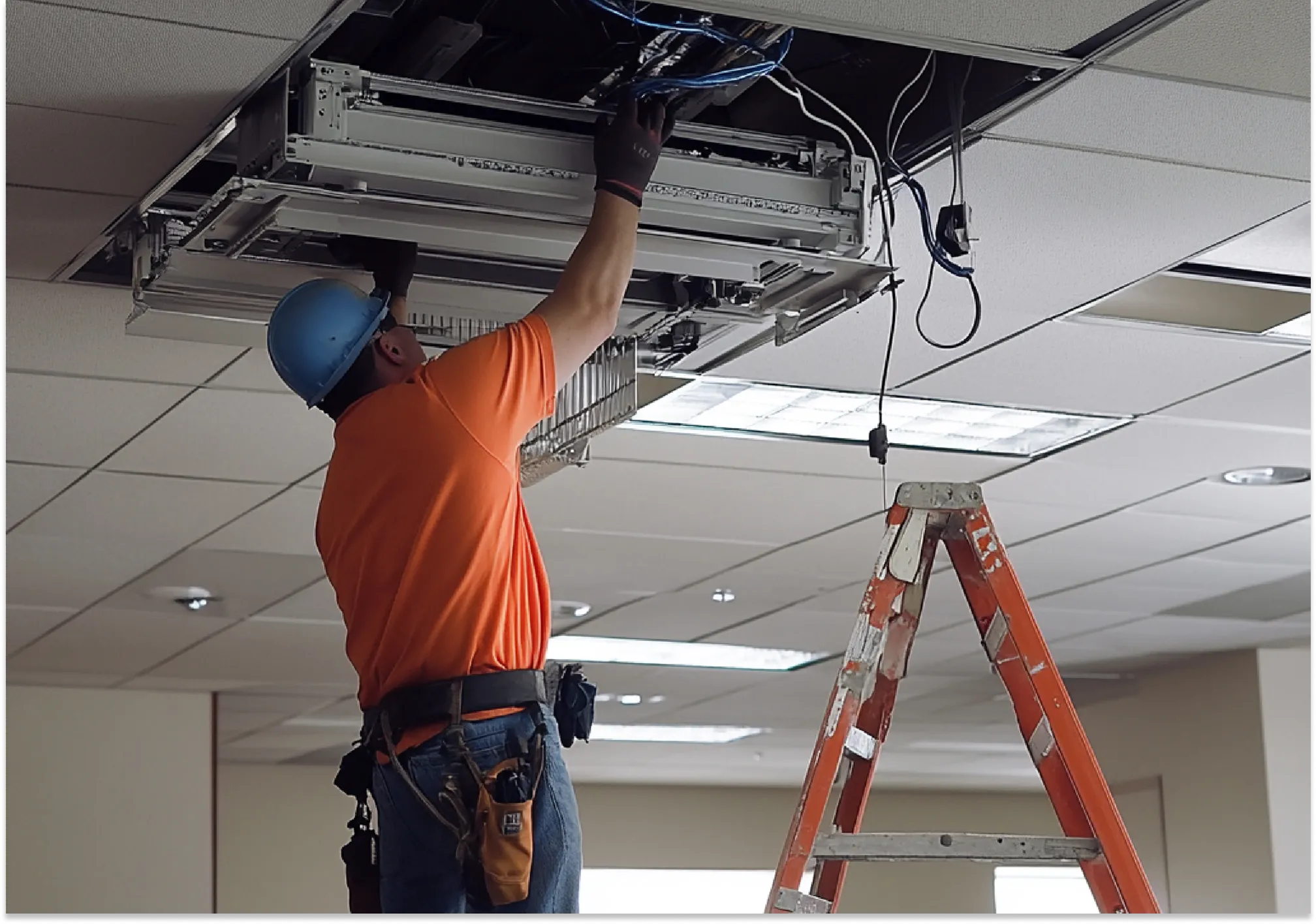 Electrician or HVAC worker standing on a ladder servicing a commercial ceiling cassette air conditioning system.