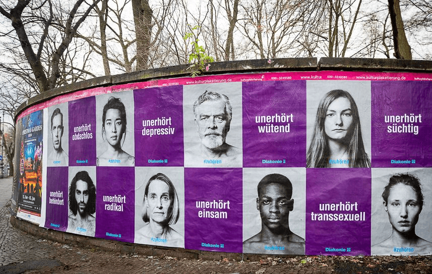 A wall of posters alternating between portraits of people and bold slogans such as “Outrageously angry,” “Outrageously lonely,” “Outrageously transgender,” and others. The photo was taken by Kathrin Harms. Image rights are held by Diakonie.