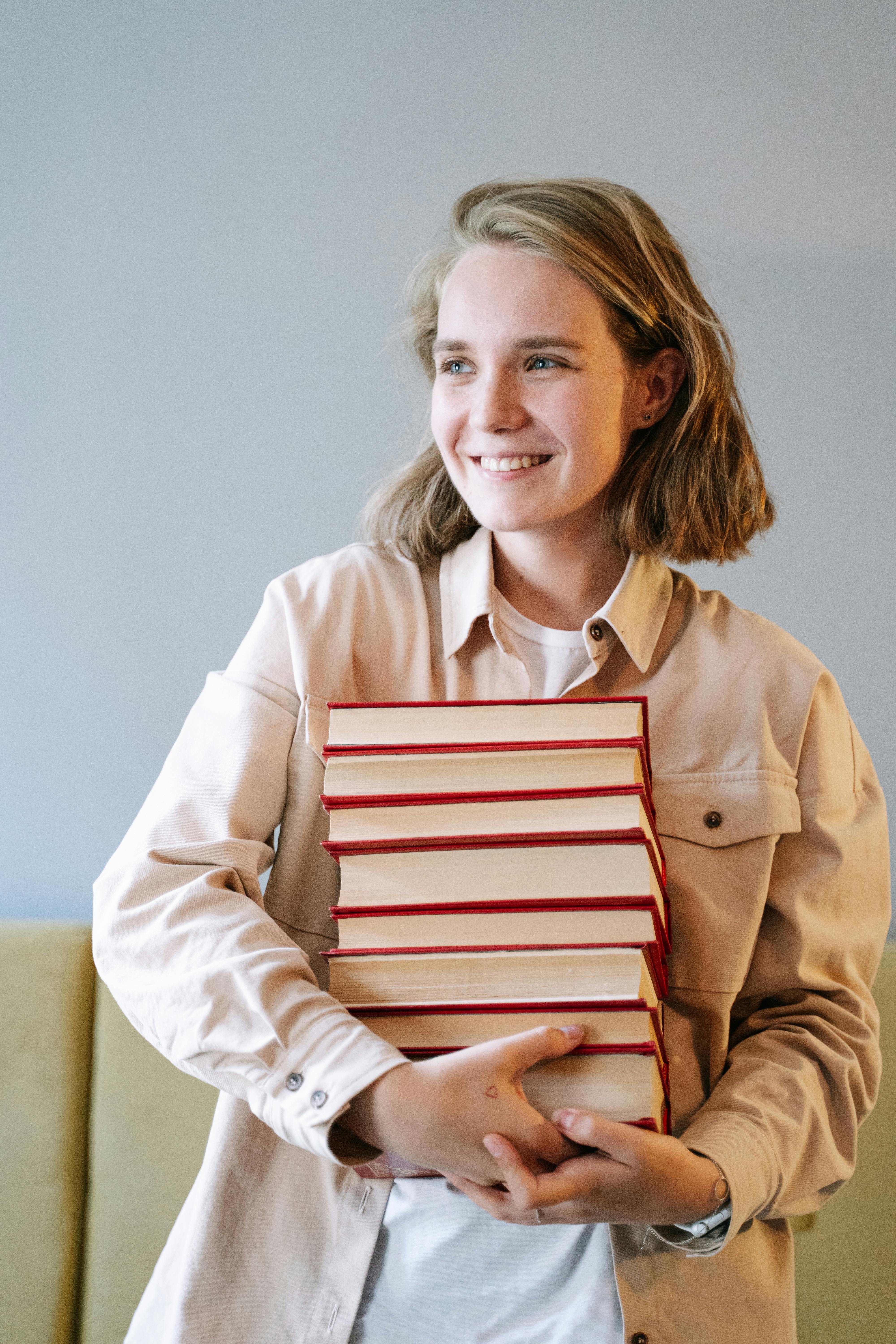 Person smiling while holding stacked books