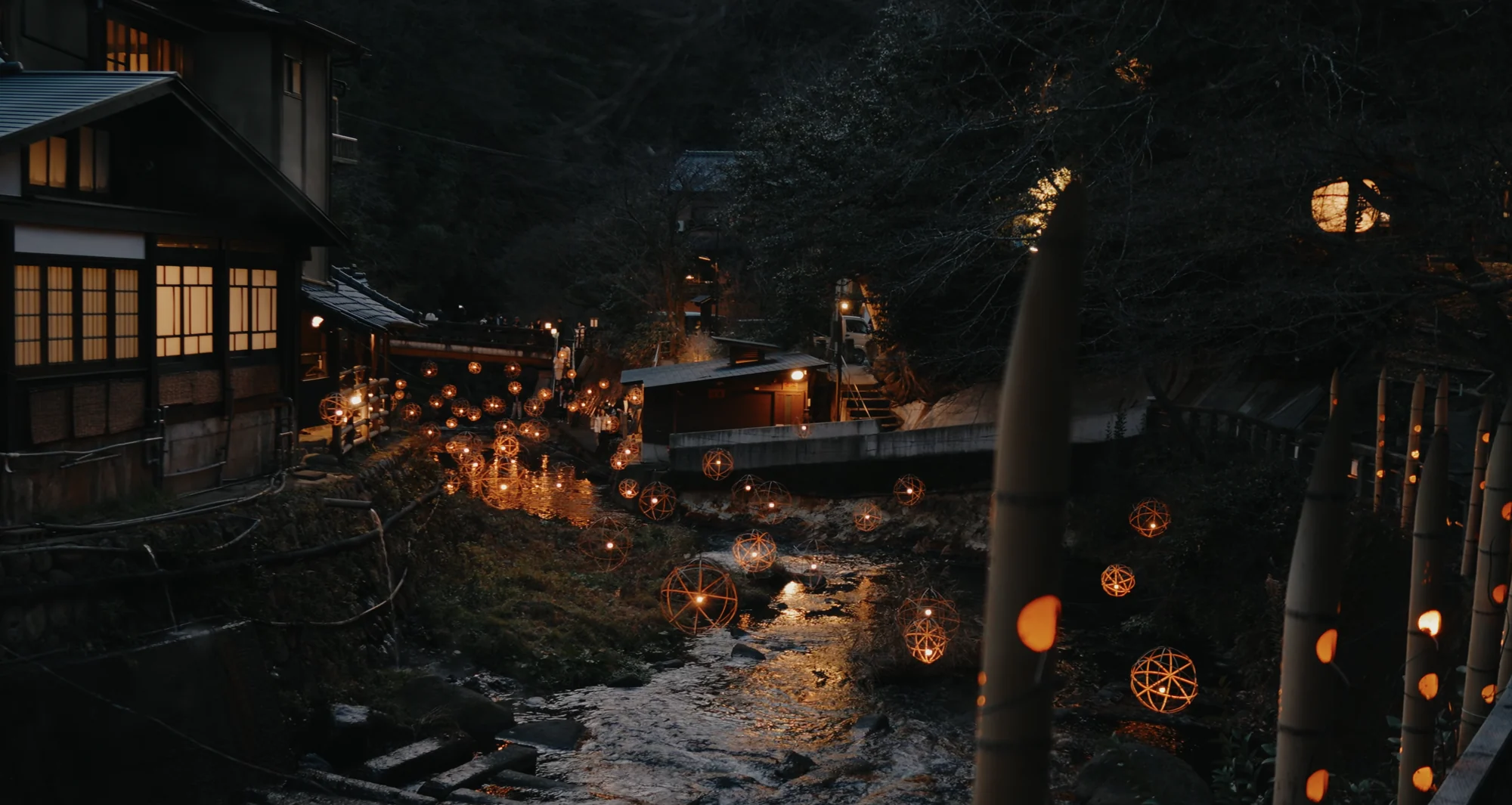 Yuakari lantern spheres massed along the riverbank below a lit timber inn