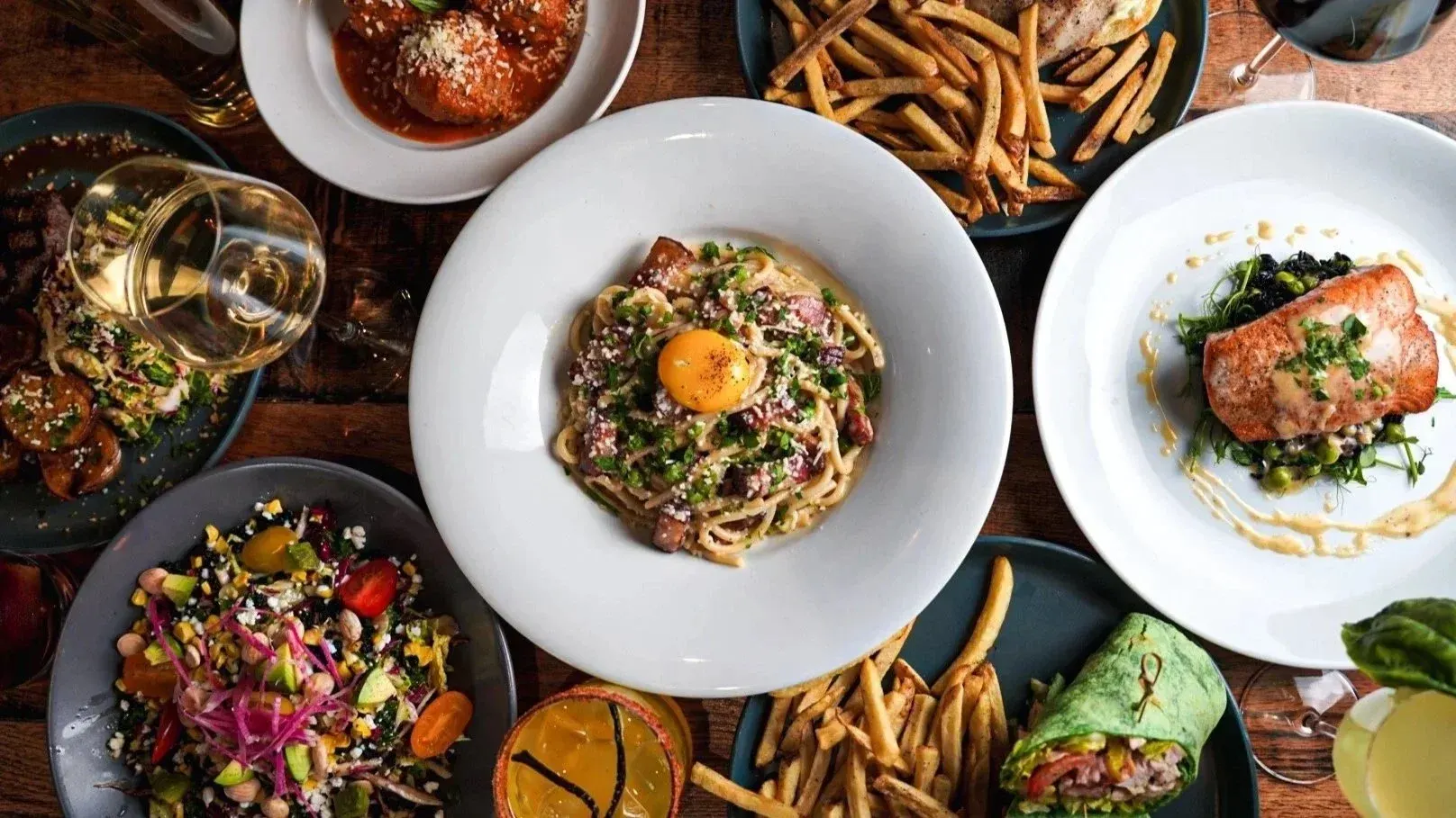 Carbonara, salmon and fries spread on a wooden table
