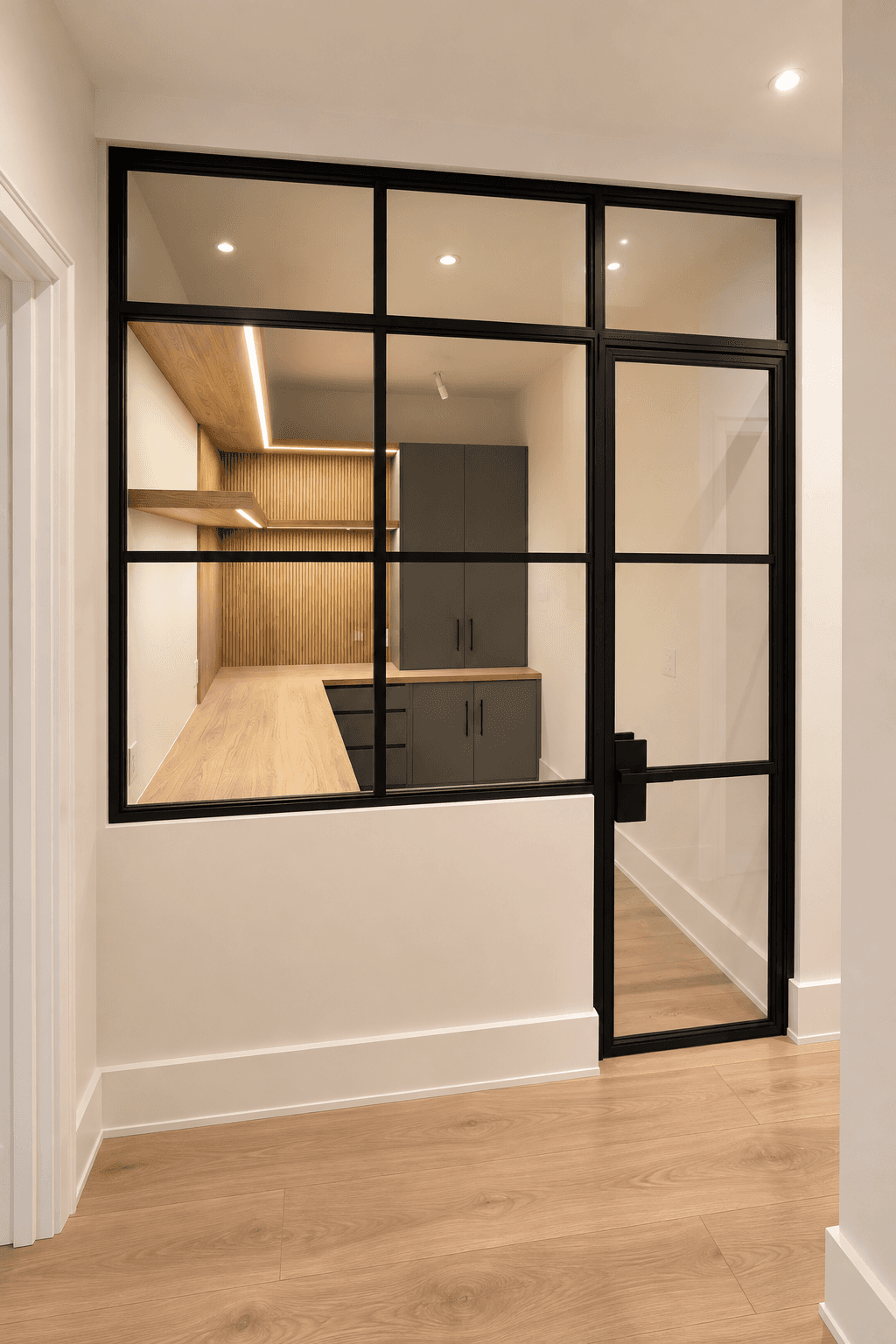Black steel-framed glass partition and door overlooking a modern workspace with warm oak finishes.