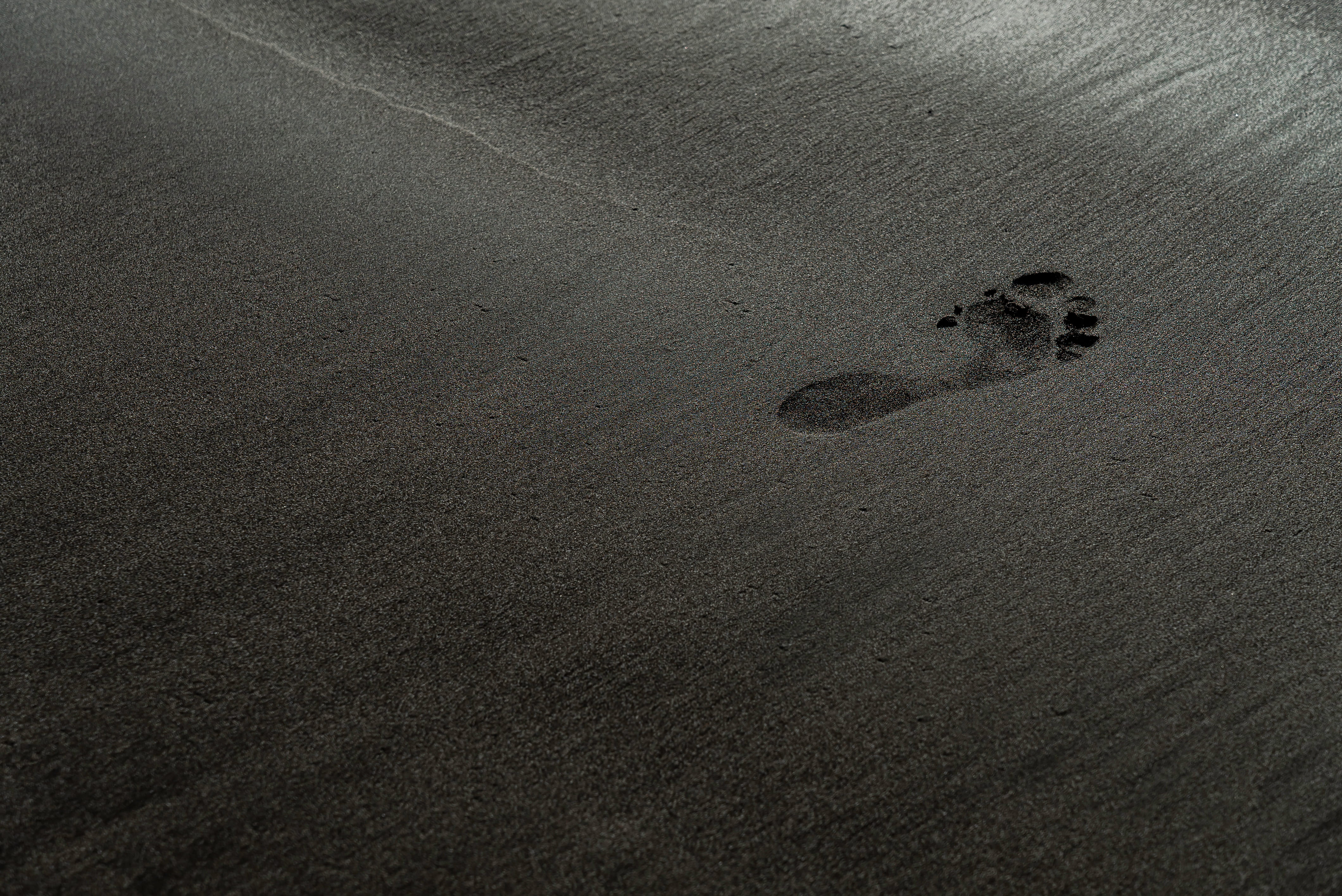 A single human footprint in dark sand.