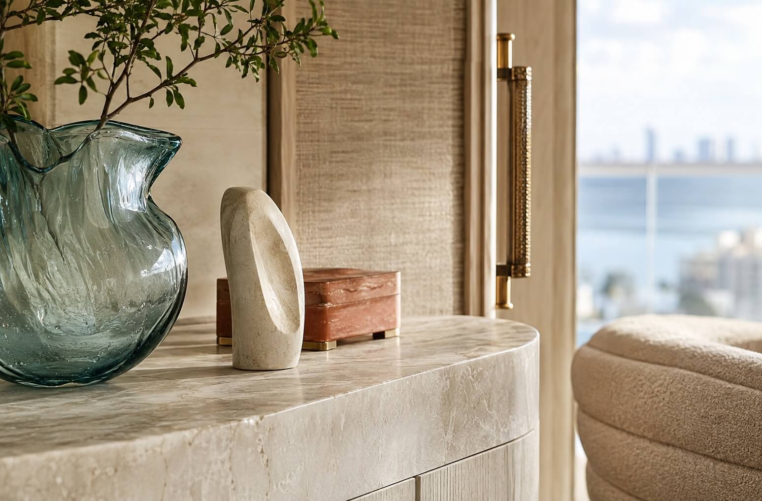 Close-up of a luxury penthouse console styled with sculptural objects, a hand-blown glass vase and waterfront views.